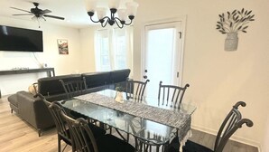 Ein Essbereich mit einem Tisch mit Glasplatte, umgeben von Stühlen, einem Deckenventilator und einem an der Wand montierten Fernseher.