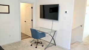 Ein Zimmer mit einem Glastisch, einem blauen Stuhl, einem an der Wand montierten Flachbildfernseher und einer Tür zu einem weiteren Raum.