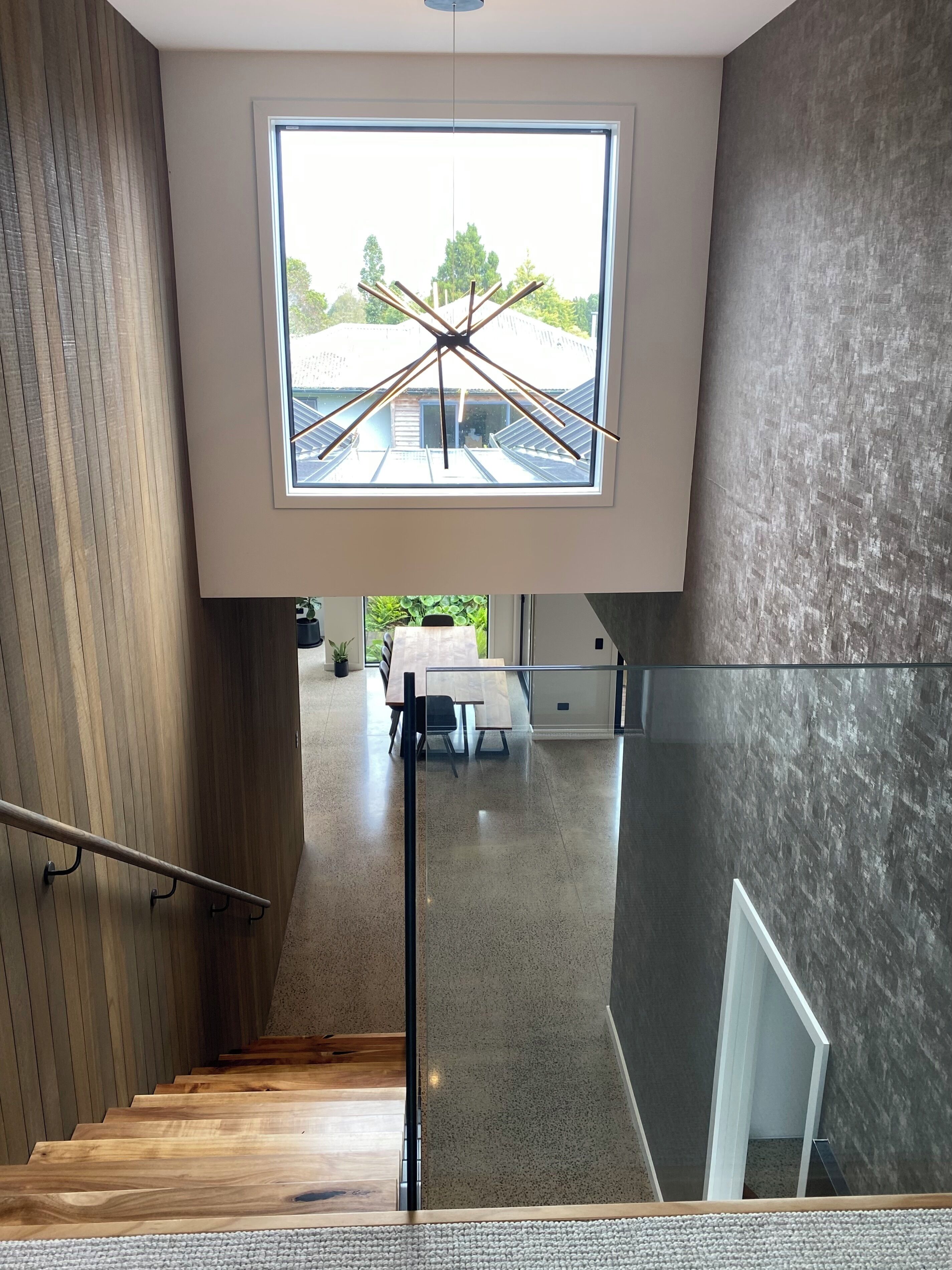 A modern interior with a staircase leading to a dining area, a large window with a view, and a mix of wood and concrete walls.