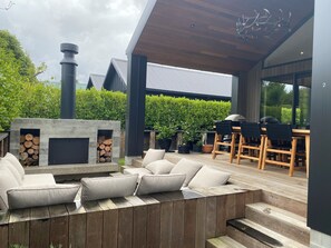 An outdoor patio area with a built-in fireplace, seating, and a grill. - Modern Retreat in Lynmore, Rotorua (Rotorua)
