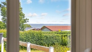 A view through a window of a property with a red-roofed building, a green hedge, and a body of water in the distance. - "Marret" - 275m from the sea by Interhome (Hejls)