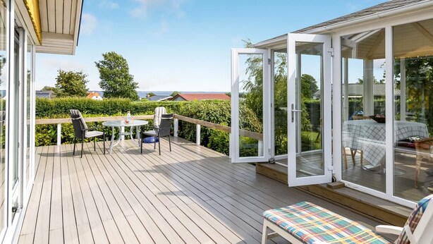 A wooden deck with a table and chairs, a bench, and a glass-enclosed room with a sofa. - "Marret" - 275m from the sea by Interhome (Hejls)