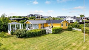 A yellow house with a glass conservatory, surrounded by a well-maintained lawn and dense greenery. - "Marret" - 275m from the sea by Interhome (Hejls)