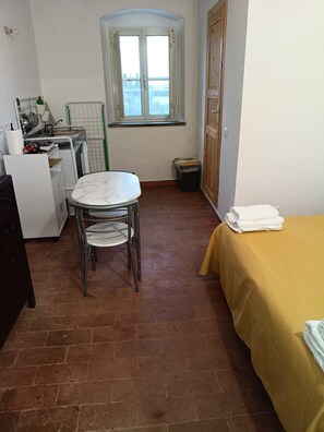 Cocina compacta con una mesa y sillas, una ventana con vistas, una cama con colcha amarilla y un cubo de basura.