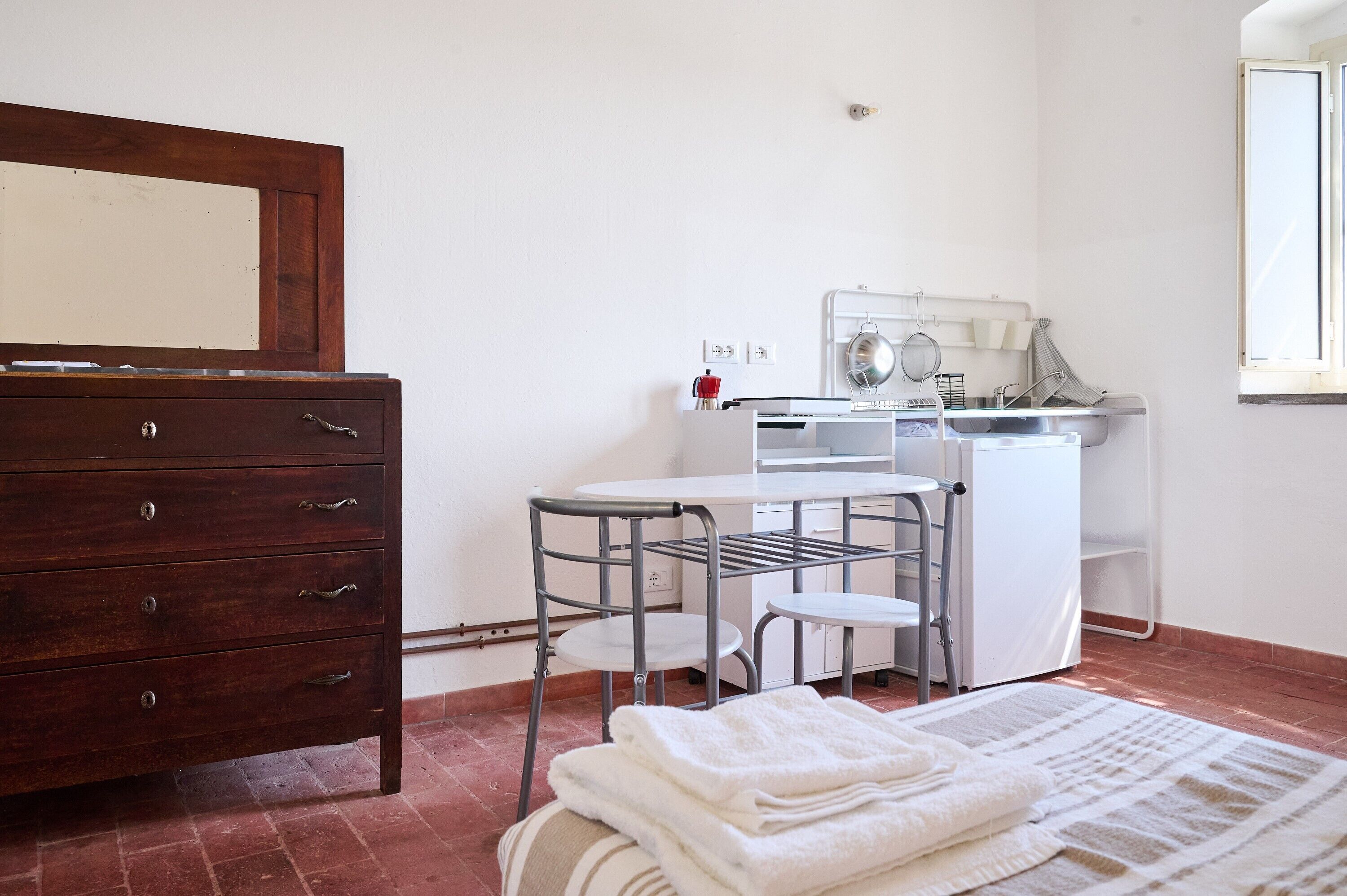 A small, clean room with a wooden dresser, a metal chair, a white table, and a washing machine.
