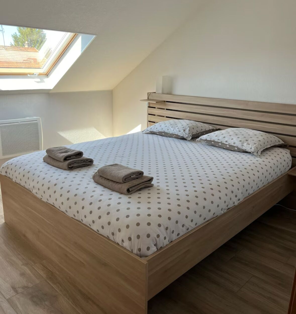 Ein Schlafzimmer mit schrägen Wänden, einem Bett mit einem Punkte-Bettbezug, zwei Kissen und zwei gefaltete Handtücher auf dem Bett.