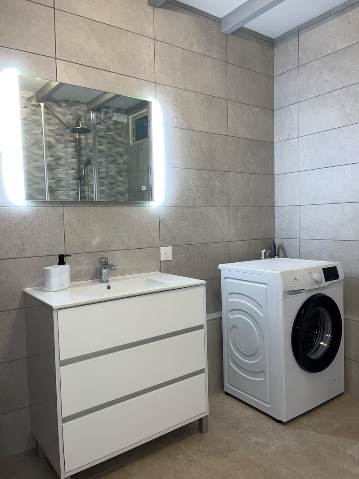A modern bathroom with a white vanity, a built-in shower, and a front-loading washing machine.