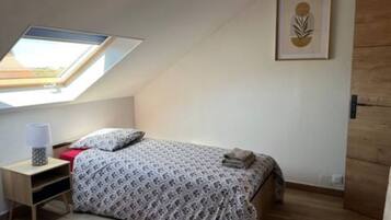 Un dormitorio con tragaluz, una cama con ropa de cama estampada, una mesita de noche con lámpara y una obra de arte enmarcada en la pared.