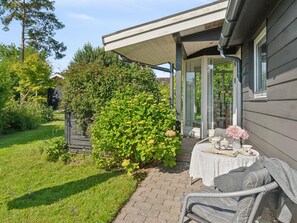 Een overdekt terras met een tafel en stoelen, omringd door groen en een huis.