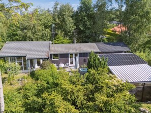 Een huis met twee verdiepingen, een schuin dak, grote ramen en een patio met tuinmeubilair.