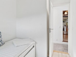 Een slaapkamer met een bed, een deur naar een gang en een kleine tafel met een stoel.