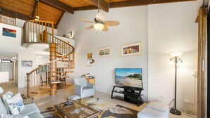 Un salón amplio con una escalera de madera, un televisor de pantalla plana grande y una zona de estar cómoda.