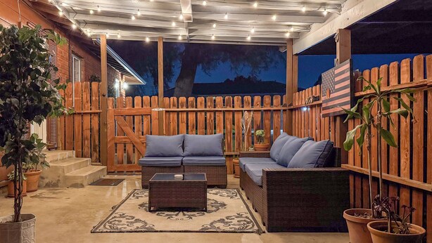 Un espace extérieur aménagé en patio, avec une clôture en bois, deux canapés avec des coussins, une table basse et des plantes en pot.