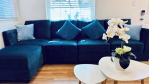 Un salon moderne avec un canapé d’angle vert foncé, une table ronde blanche et un vase rempli de fleurs blanches.