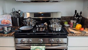 Une cuisine équipée d’une cuisinière, d’un four et d’un four à micro-ondes en acier inoxydable. On y trouve des casseroles et des poêles sur la cuisinière, une planche à découper avec des légumes et un livre de recettes sur le comptoir.