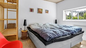 A modern bedroom with a bed, a red chair, a wooden shelf, and a window with a view.