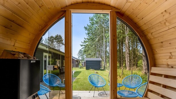 A circular wooden room with a large window, a black grill, and two blue chairs.