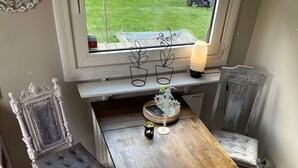 A dining area with a wooden table, two upholstered chairs, a black and white striped rug, and a window with a view of a garden.