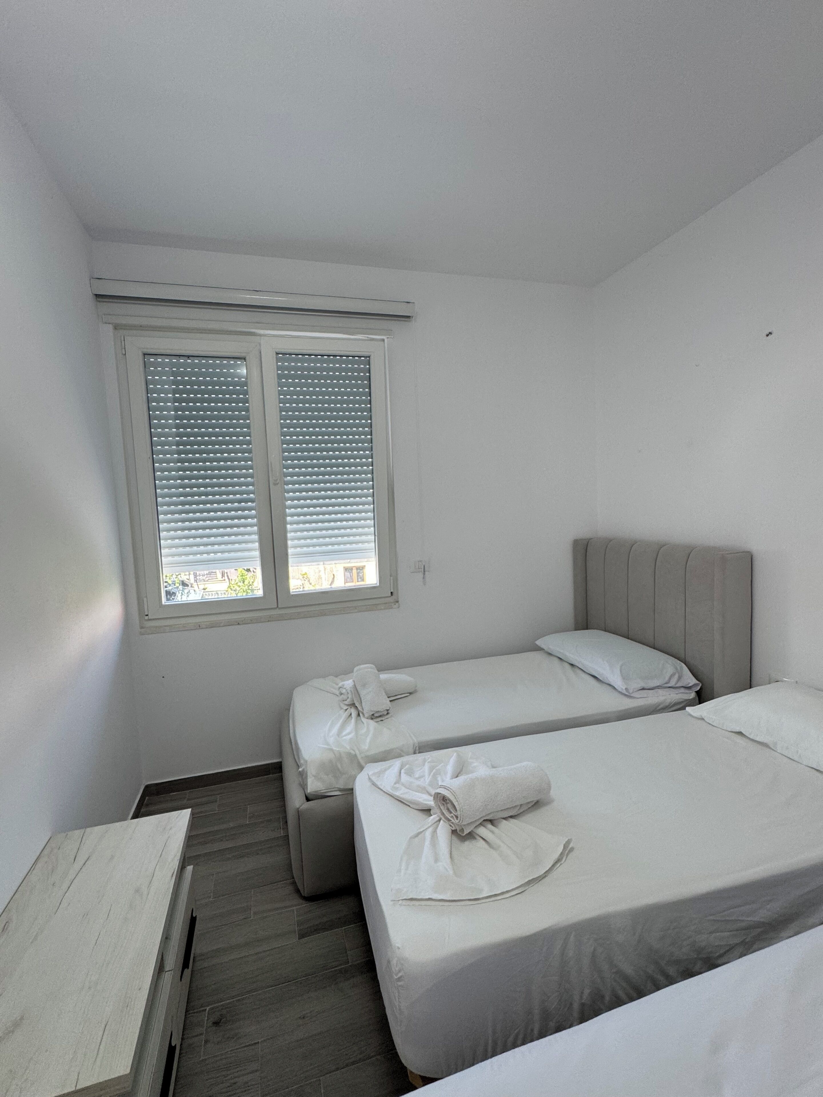 Ein Zimmer mit zwei Betten, einem Fenster mit Jalousien und einer Holzbank.