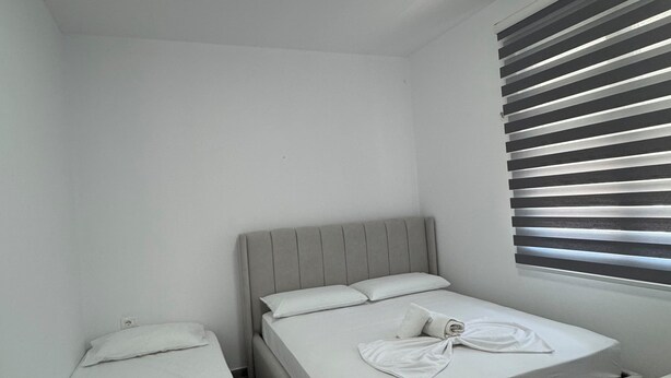 A small, clean room with two beds, a ceiling light, and a window with blinds. - Charming 3-bedroom Villa in lovely Shkodër with AC (Shkodër)