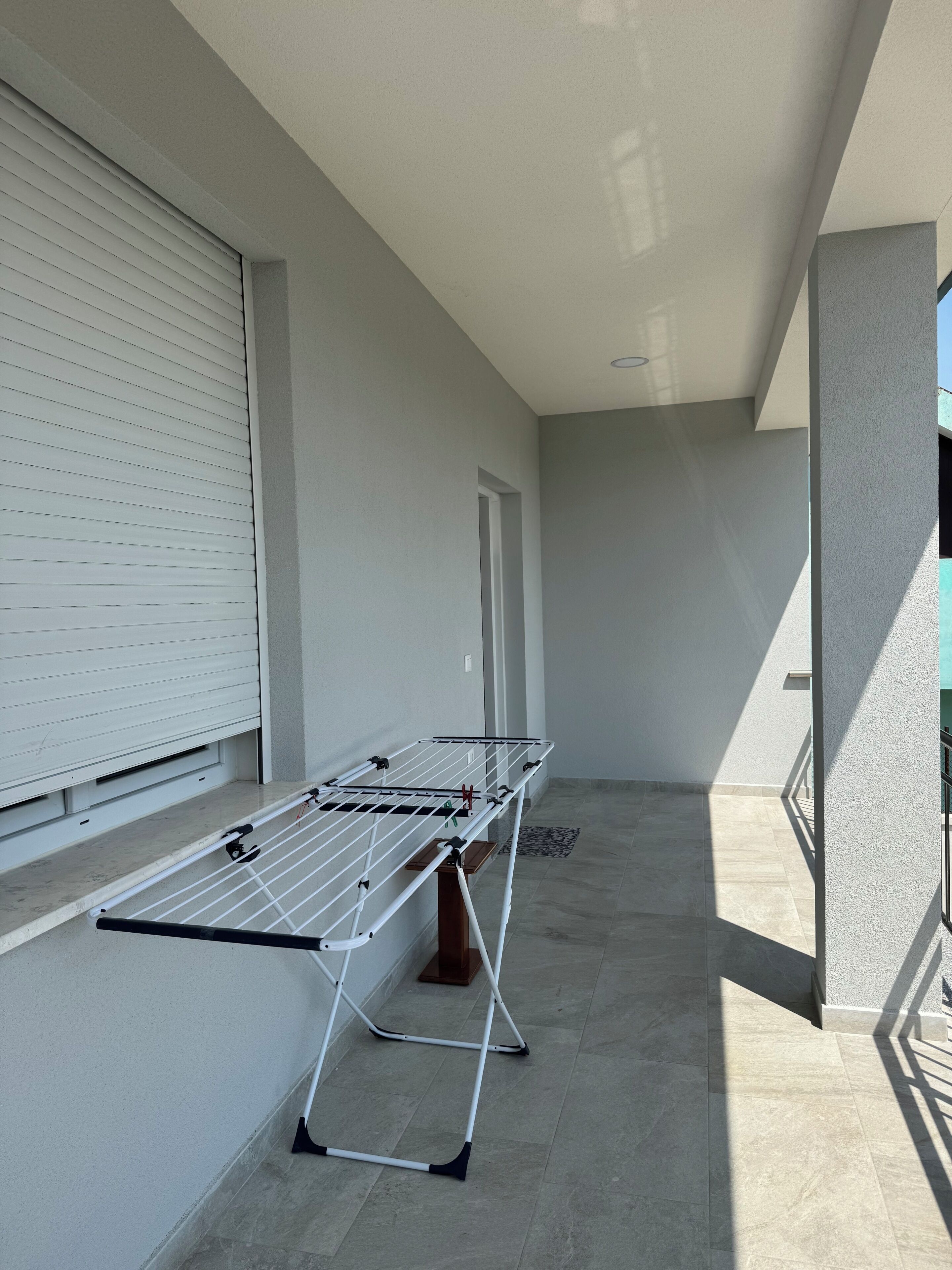 A balcony with a drying rack, a window with blinds, and a door.