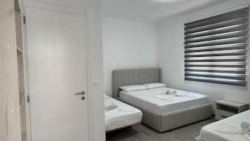 A bedroom with two beds, a wardrobe, a bedside table, and a window with blinds.