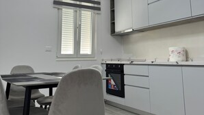 A modern kitchen with a dining area, featuring a built-in oven, white cabinetry, and a window with blinds. - Charming 3-bedroom Villa in lovely Shkodër with AC (Shkodër)