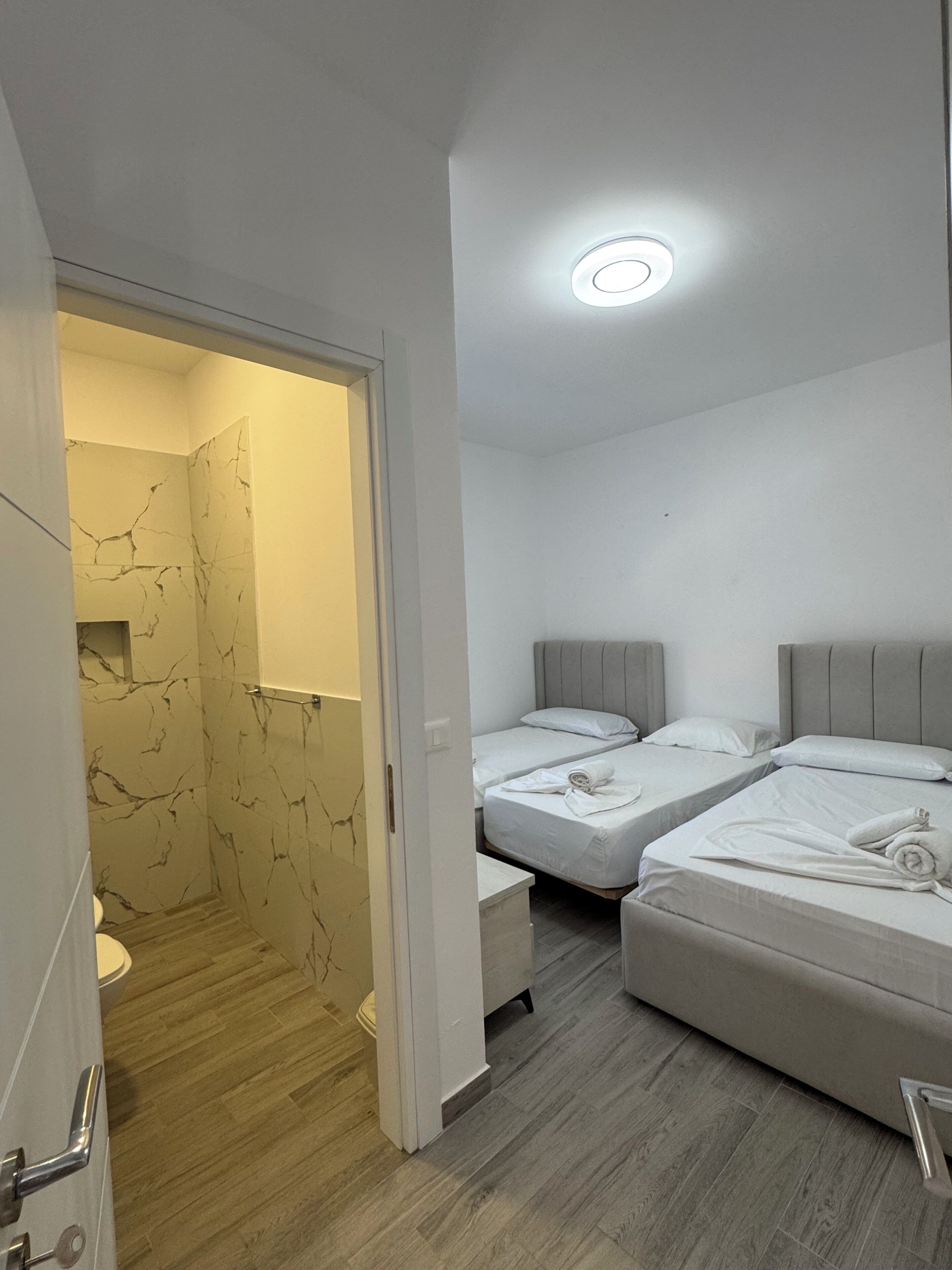A hotel room with a bathroom, two beds, and a shower area.