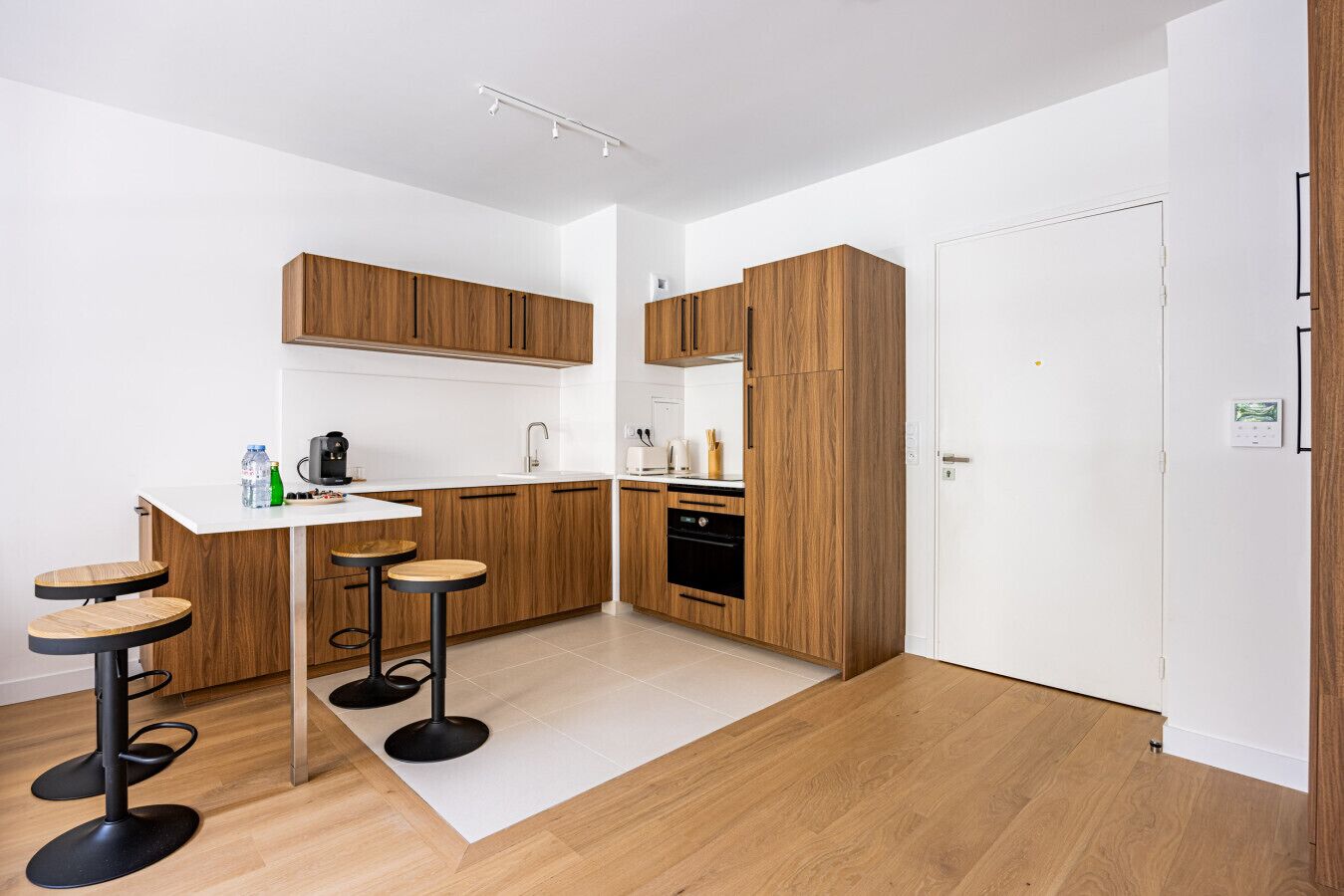 Una cucina moderna con mobili in legno, un piano di lavoro bianco e due sgabelli da bar.