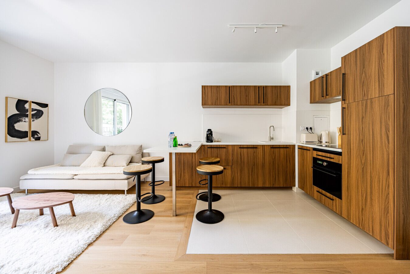 Una cucina moderna con mobili in legno, un piano di lavoro bianco e un forno integrato. Sopra il lavello c'è uno specchio rotondo e un piccolo tavolo con sgabelli.