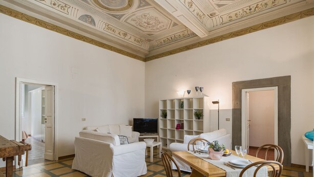 Een woonkamer met een bank, een televisie, een boekenkast en een eettafel met stoelen.