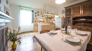 A well-lit kitchen with a dining table set for two, featuring a tiled backsplash, wooden cabinets, and a hanging light fixture. - Casa Brezza del Gabberi by Interhome (Camaiore)