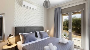 Ein modernes Schlafzimmer mit einem großen Bett, grauer Bettwäsche, einem Kopfteil, einer Klimaanlage, einer Nachttischlampe und Blick ins Freie durch eine Glasschiebetür.