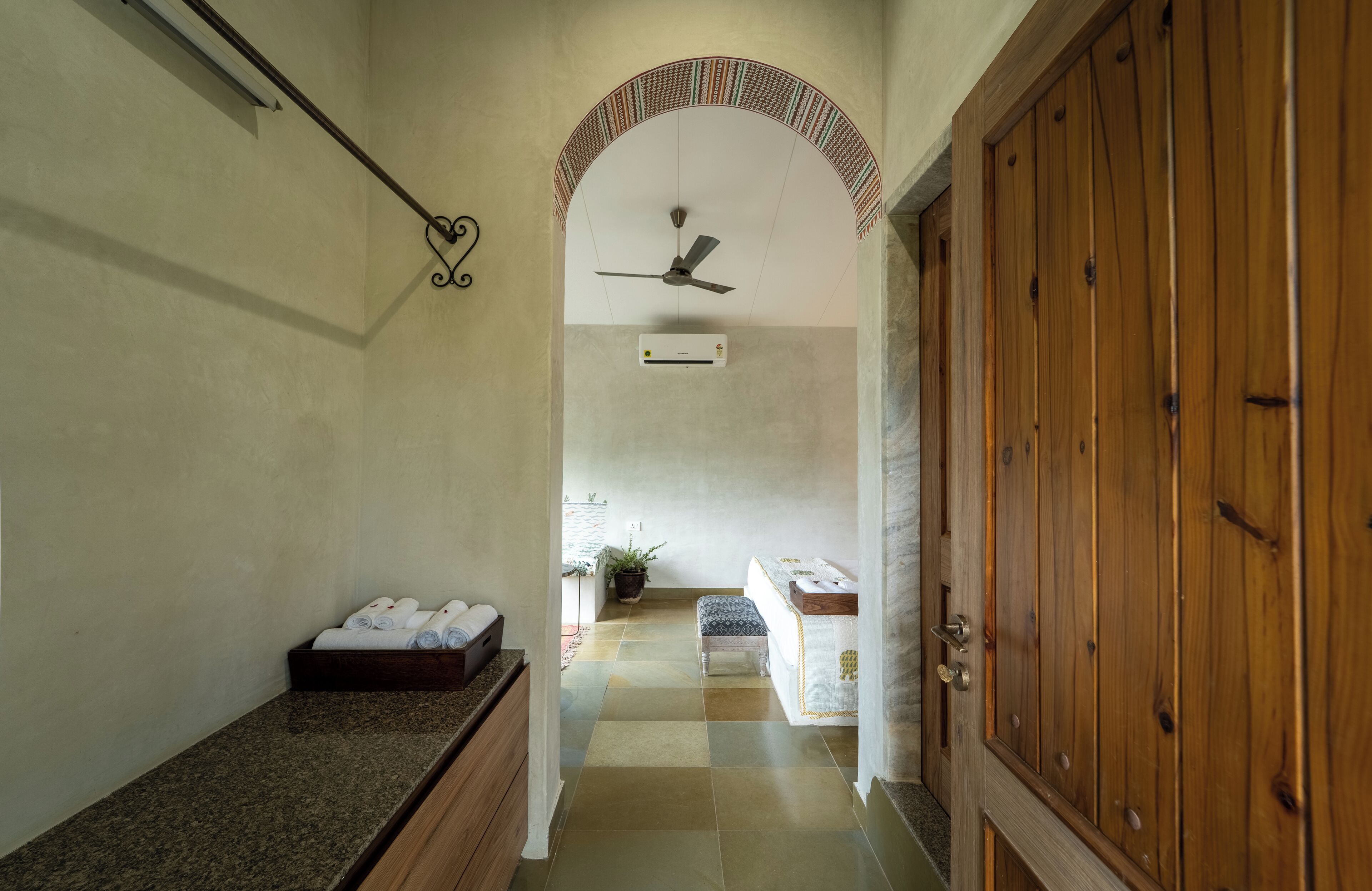 Un couloir avec un ventilateur de plafond, une porte en bois, un banc et une petite table sur laquelle sont posées des serviettes.