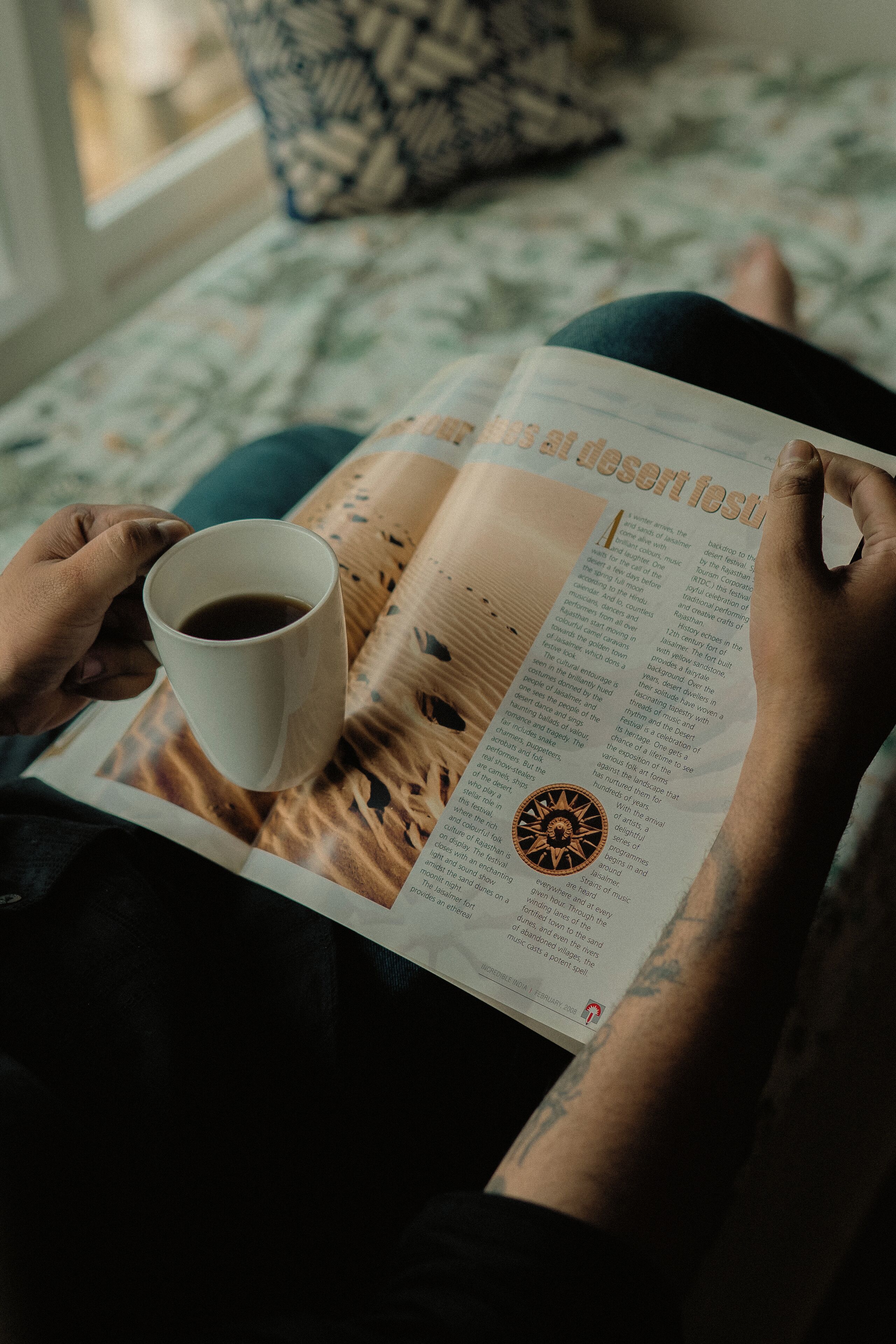A person reading a magazine with a coffee cup.