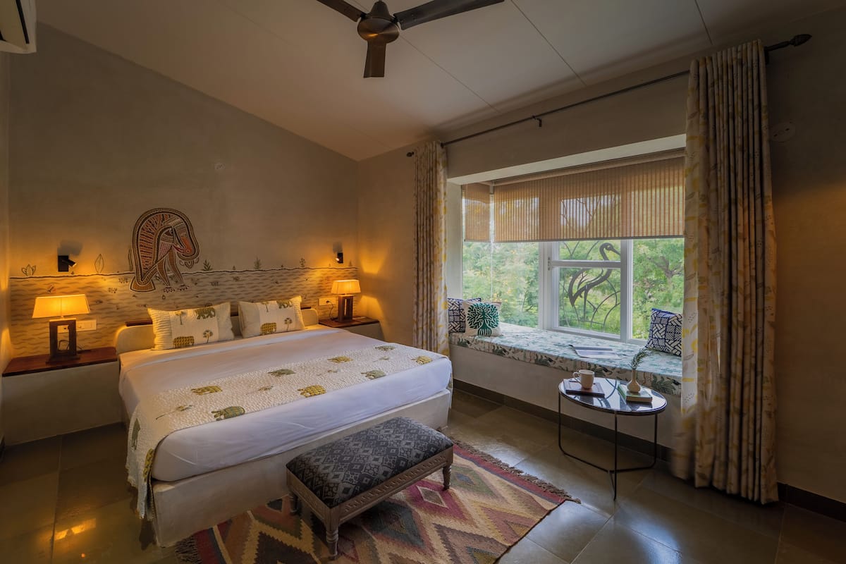 A bedroom with a large bed, bedside lamps, a window with curtains, a small table, and a ceiling fan.