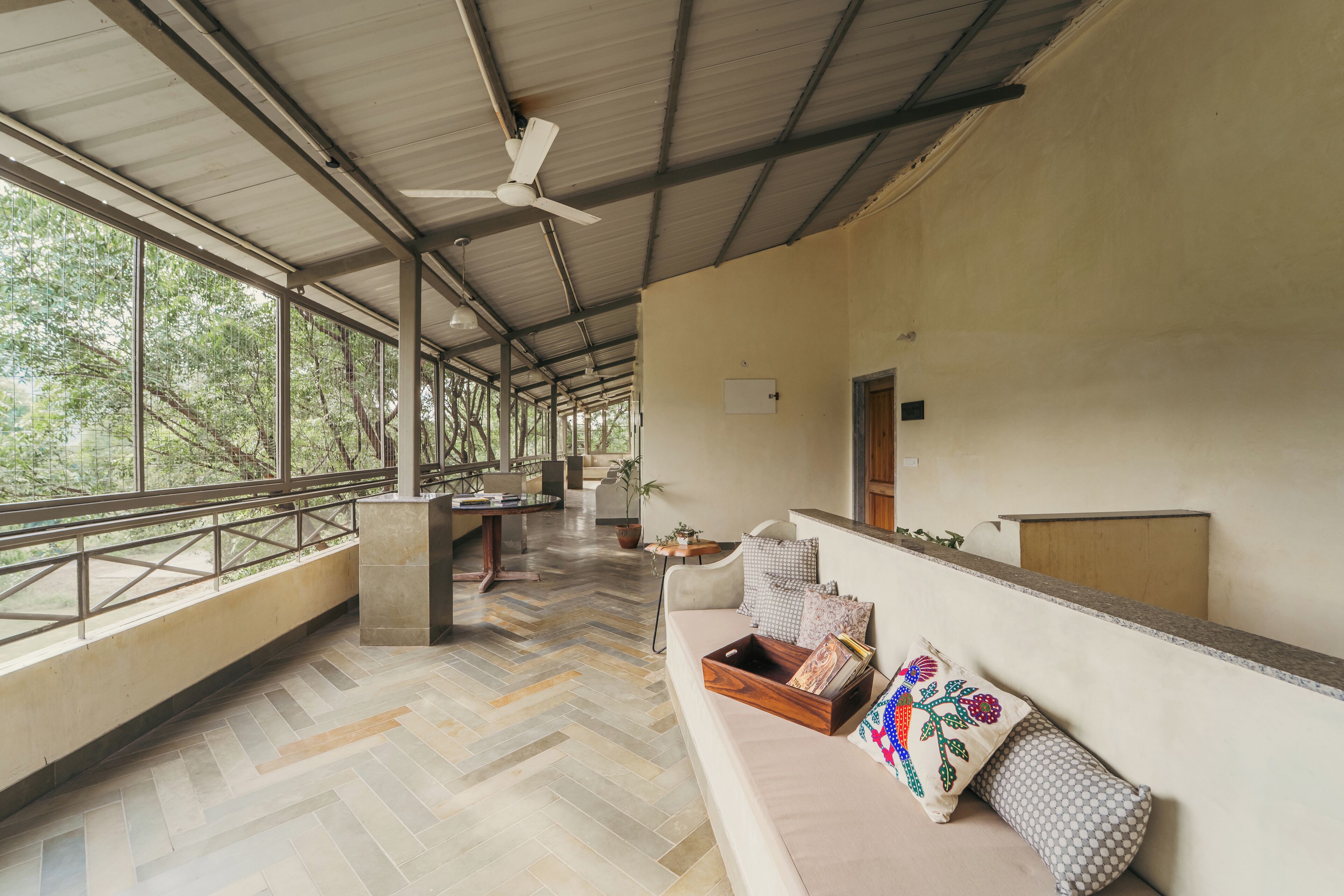 A spacious room with a herringbone floor, a sofa with decorative pillows, a small table with a plant, and a ceiling fan.
