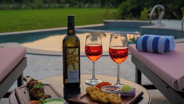 A table with a bottle of wine, two glasses of red wine, a plate of food, and a poolside view. - Tehla Bagh (Talab)