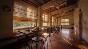 A spacious dining area with wooden tables and chairs, large windows allowing natural light, and a ceiling fan. - Tehla Bagh (Talab)