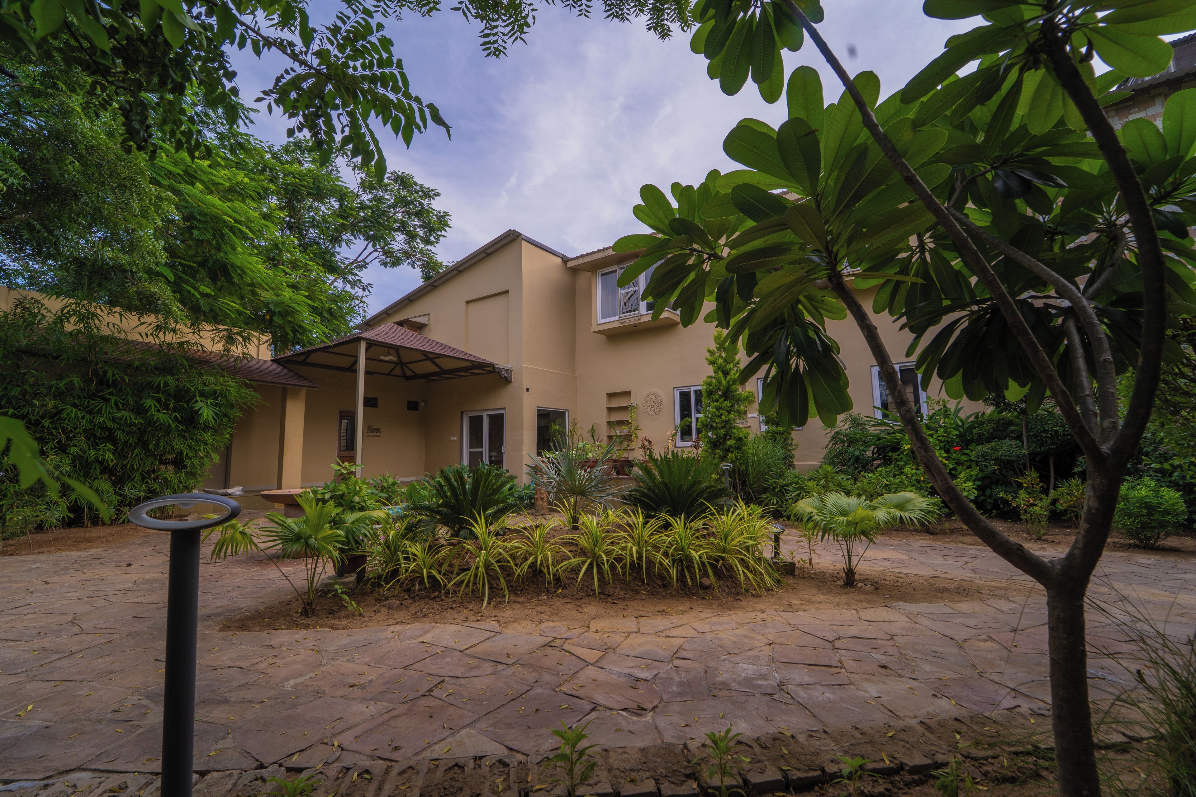A building with a tiled patio, surrounded by various plants and trees.