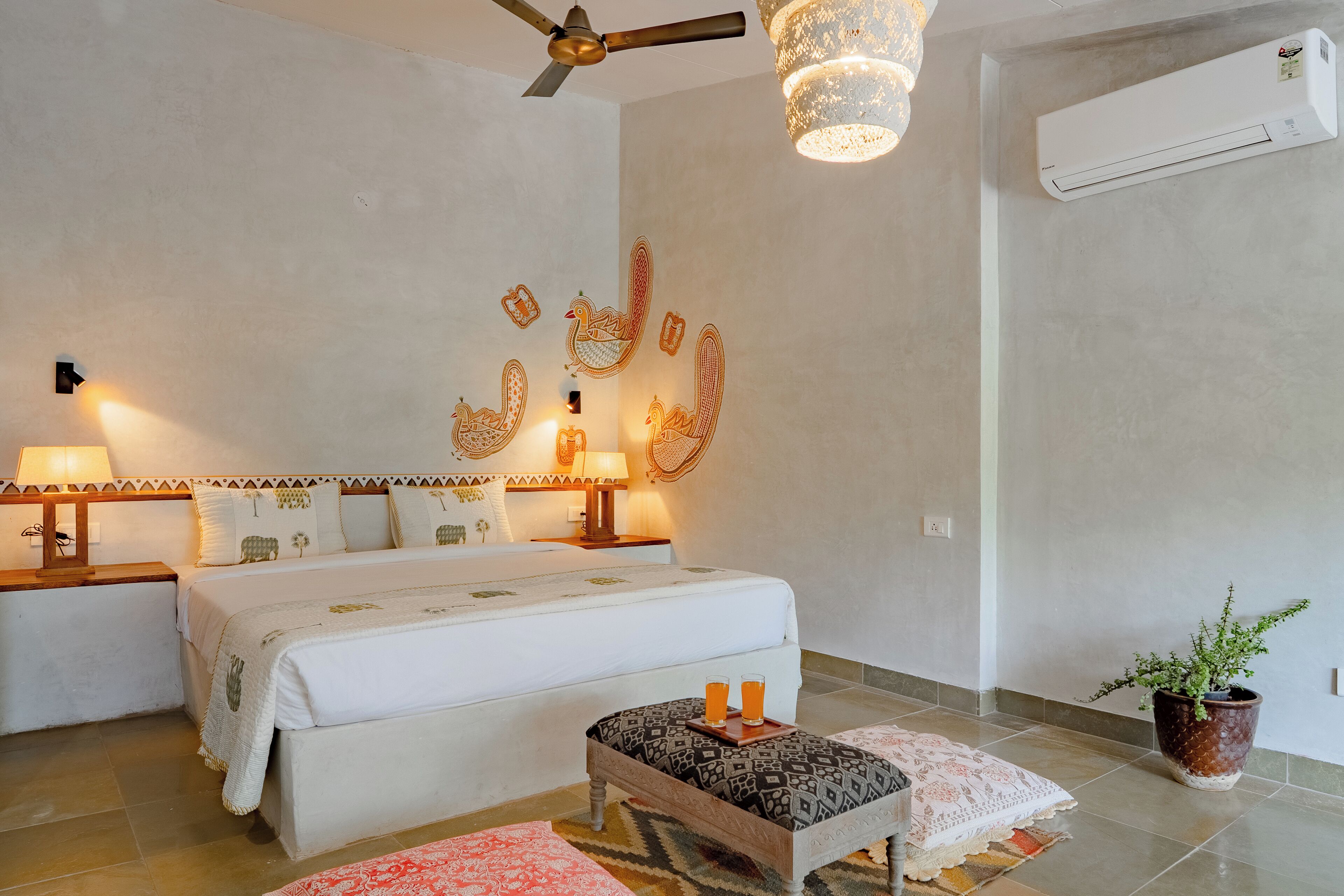Habitación de hotel con cama, lámparas de noche, ventilador de techo, equipo de aire acondicionado y planta en maceta.