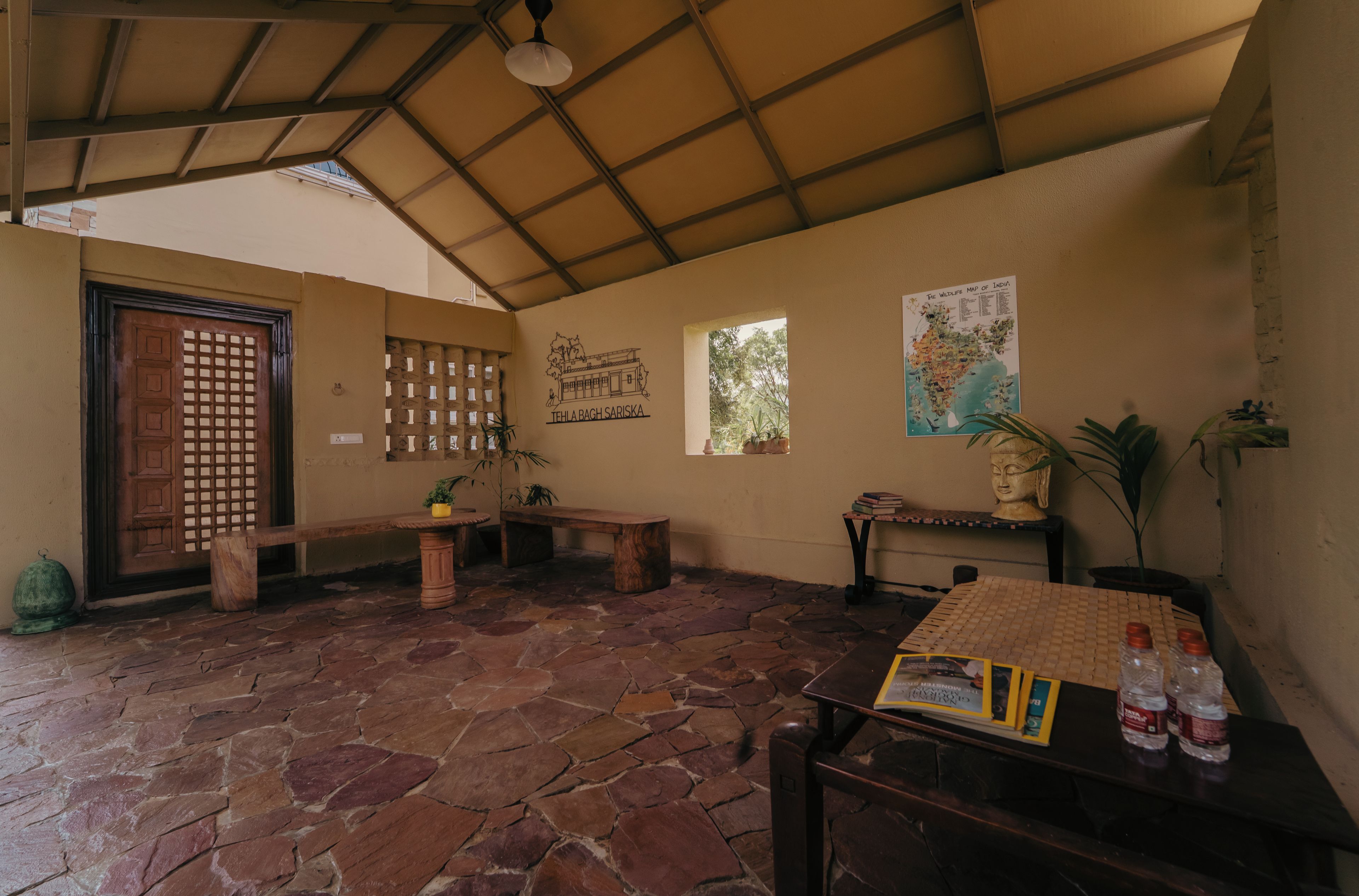 Une pièce au sol en pierre, avec une porte en bois, un banc, une table sur laquelle se trouvent des livres et des bouteilles, et une fresque murale.
