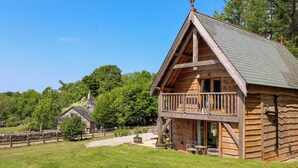 A wooden cabin with a balcony, named 'Pucklechurch', surrounded by a grassy area and trees. - Pucklechurch (Newton Abbot)