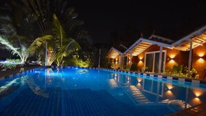 A nighttime swimming pool with tiled flooring and surrounding palm trees. - Golden Rice Resort (Candolim)