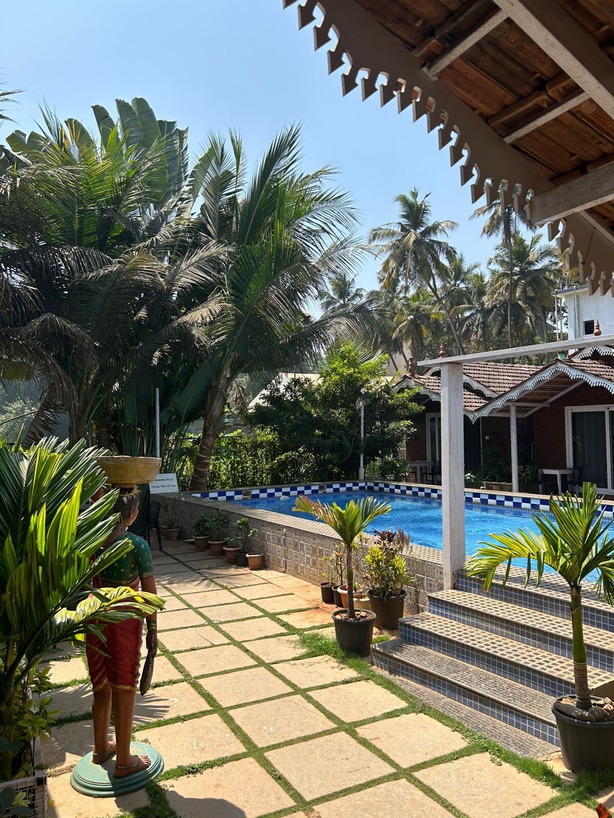 A pool area with a tiled deck, palm trees, and a person carrying a basket.