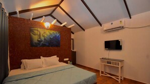 A bedroom with a bed, a painting on the wall, a TV, and an air conditioning unit. - Golden Rice Resort (Candolim)