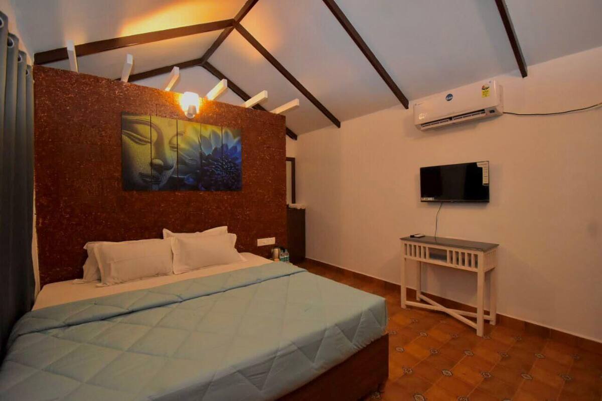 A bedroom with a bed, a painting on the wall, a TV, and an air conditioning unit.