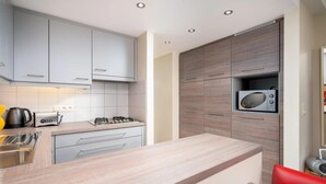 Una cocina moderna con gabinetes grises, un microondas, una estufa a gas y una silla roja.