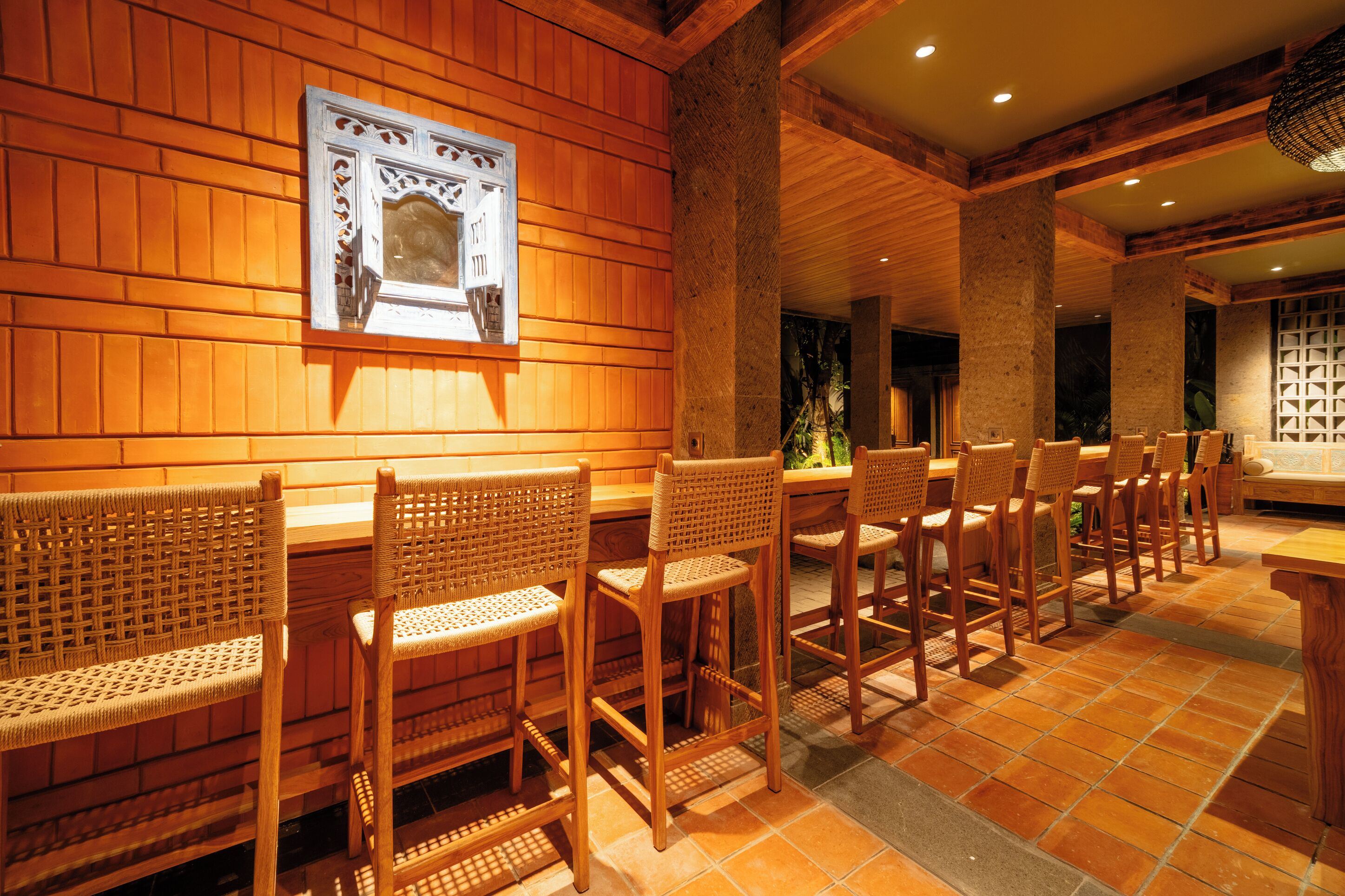 A restaurant with wooden walls and a tiled floor, featuring wicker chairs and a wooden bar.