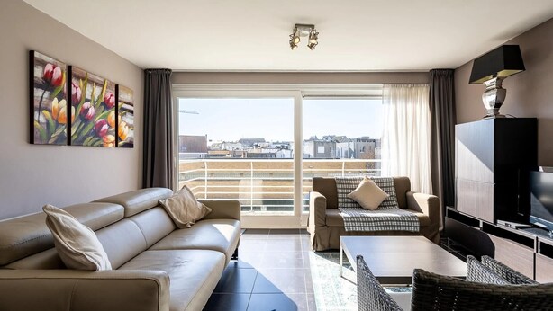 Een moderne woonkamer met een bank, een salontafel en een televisie. Er is een balkon met uitzicht over de stad.